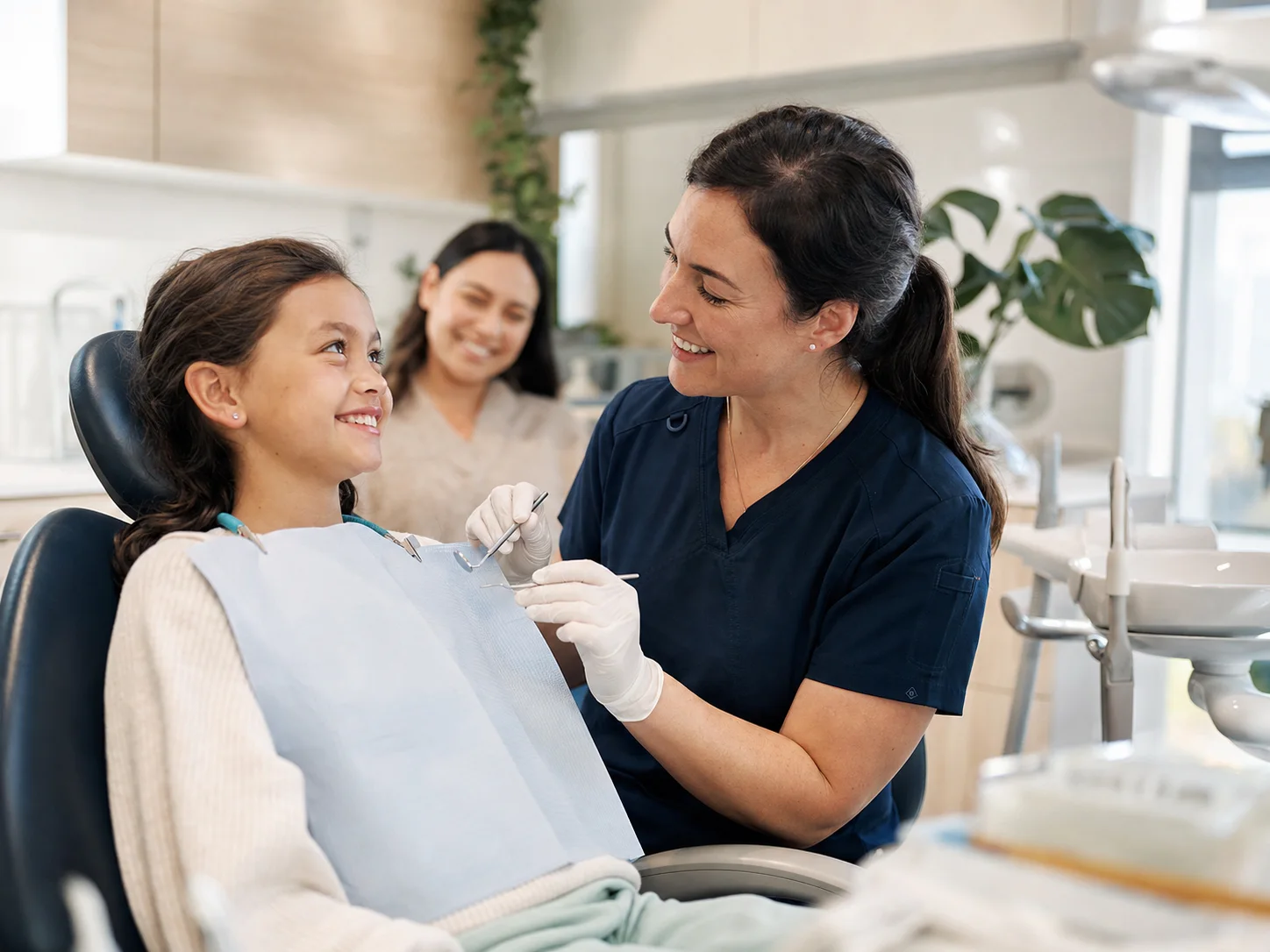 A dentist reassuring a smiling child during a dental appointment while the child’s parent looks on.